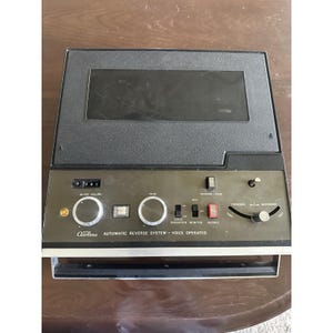 May include: Vintage Airline automatic reverse system with a black and silver face. The device has several knobs and buttons, including AC off/volume, tone, and forward/backward controls. The text "Airline AUTOMATIC REVERSE SYSTEM - VOICE OPERATED" is printed on the front.