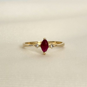 May include: A gold ring featuring a marquise-shaped ruby gemstone and two smaller diamond accents.