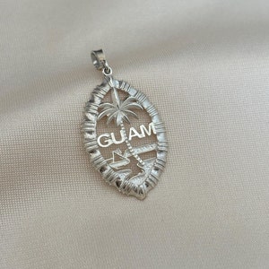 May include: Silver pendant featuring a palm tree and the word "GUAM" in a stylised oval shape.
