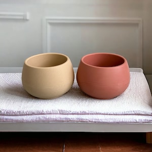 May include: Two small, round, ceramic planters. One is beige and the other is terracotta.