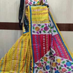 May include: A vibrant, hand-painted saree with a yellow base and colorful floral and geometric patterns. The saree features a mix of pink, blue, and white accents, with a black border on one side. The design is displayed on a mannequin.