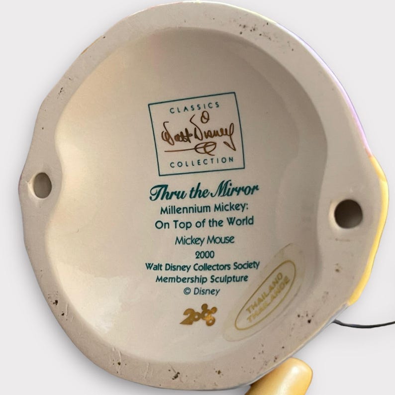 May include: A ceramic sculpture base with text that reads "Thru the Mirror" and "Millennium Mickey: On Top of the World." The sculpture is a Walt Disney Collectors Society Membership Sculpture from 2000, featuring Mickey Mouse.