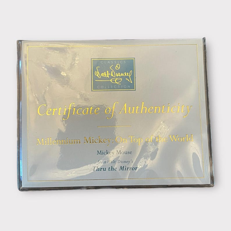 May include: A certificate of authenticity from the Walt Disney Classics Collection. The certificate is in a clear plastic sleeve. The text on the certificate reads "Certificate of Authenticity" and "Millennium Mickey: On Top of the World".