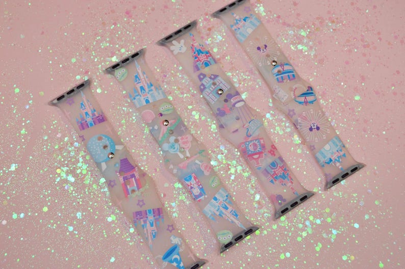 May include: Four clear silicone Apple Watch bands with a pastel pink, blue, and purple print of Disney castles and other icons.