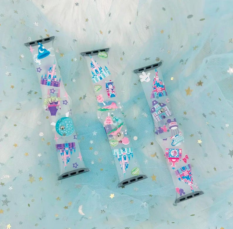May include: Three colorful Apple Watch bands with Disney park designs. The bands feature a variety of characters and attractions, including Mickey Mouse, Cinderella's Castle, and Space Mountain.