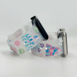 May include: Two white silicone watch bands with colorful cartoon prints. One band features a castle and Mickey Mouse, the other features a castle and a green alien. Both bands are compatible with Apple Watch.