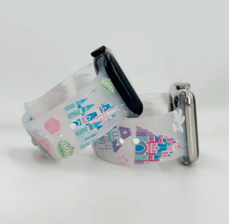 May include: Two white silicone watch bands with colorful cartoon prints. One band features a castle and Mickey Mouse, the other features a castle and a green alien. Both bands are compatible with Apple Watch.