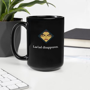 May include: Black ceramic coffee mug with a white graphic of a character's face with the text "Lae'zel disapproves."