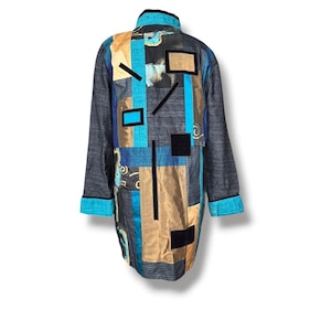 May include: A long-sleeved jacket featuring a patchwork design with panels of charcoal gray, metallic gold, and bright turquoise fabric. The garment includes black rectangular accents, a high collar, and turquoise cuffs with black trim edges.