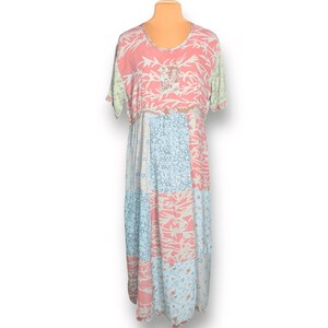 May include: A patchwork maxi dress with short sleeves. The dress features a pink bodice with white floral patterns and a lace detail. The skirt is a mix of pink, blue, and white patterned panels.