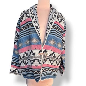 Puede incluir: Chaqueta estampada con diseño del suroeste. La chaqueta presenta una mezcla de colores, incluyendo rosa, azul, negro y blanco. Tiene cierre de botón y cuello chal. El diseño de la chaqueta incluye formas geométricas y rayas.