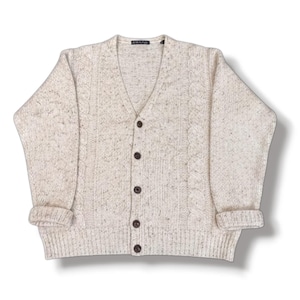 May include: A cream-colored V-neck cardigan sweater featuring a speckled texture and vertical cable knit patterns on the front panels. The garment includes five dark brown buttons down the center and ribbed cuffs at the ends of the long sleeves.
