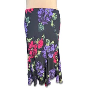 May include: A black floral skirt featuring a vibrant pattern of pink and purple flowers with green leaves. The skirt has a flowing, flared design and is made of a lightweight fabric. The floral print is eye-catching and adds a touch of elegance.