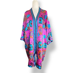 May include: A vibrant, patterned kimono in shades of pink, blue, orange, and purple. The open-front garment features a detailed floral and geometric design. The kimono is displayed on a mannequin, showcasing its flowing silhouette and colorful aesthetic.