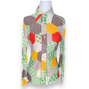May include: A long-sleeved button-down shirt with a patchwork design. The shirt features a variety of patterns and colors, including green, yellow, red, brown, and white. The shirt has a pointed collar and is displayed on a mannequin.