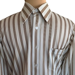 Op de afbeelding: Een overhemd met verticale strepen in bruin, wit en lichtblauw. Het overhemd heeft een puntkraag, een borstzak en is dichtgeknoopt. De stof lijkt licht van gewicht.