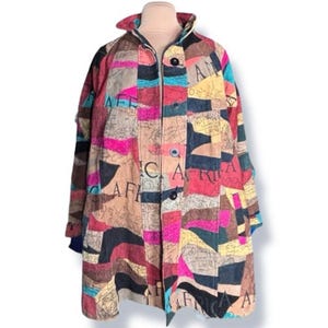 May include: A colorful patchwork coat with a collared neckline and button closure. The coat features a variety of fabric squares in shades of pink, blue, yellow, and brown, with the word "Africa" printed on some squares. The coat is displayed on a mannequin.