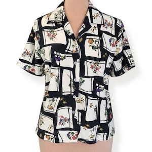 May include: Short-sleeved button-up shirt with a black and white geometric pattern. The pattern includes floral accents in various colors. The shirt has a collared neckline and is buttoned down the front.