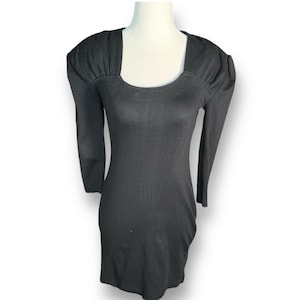 May include: A black, long-sleeved dress with a square neckline and shoulder detailing. The dress is form-fitting and appears to be made of a stretchy material. The dress is displayed on a mannequin.