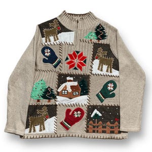 以下が含まれることがあります： ベージュのジップアップセーター。クリスマスをテーマにしたアップリケが施されたパッチワークデザイン。パッチにはトナカイ、ミトン、クリスマスツリー、雪の結晶、雪の家が含まれています。セーターはリブ編みの襟と袖口が付いています。