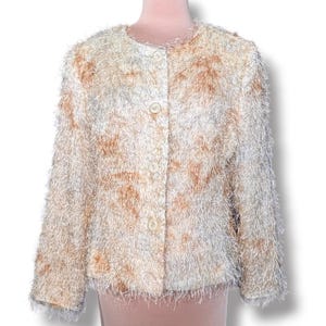 May include: A long-sleeve jacket featuring a shaggy, textured surface in shades of cream, white, and light brown. The garment has a round neckline, a straight hem, and a front button closure with four matching round buttons aligned vertically.