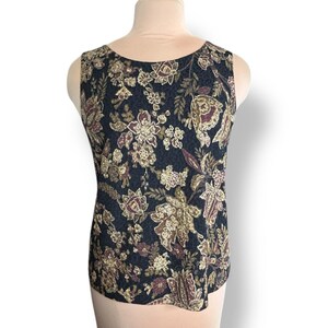 Può includere: Top senza maniche con motivo floreale. Il top presenta uno sfondo blu navy scuro con un motivo ripetuto di fiori bordeaux, beige e verde oliva. La scollatura è rotonda.