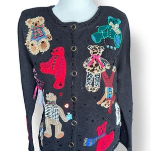 May include: Black cardigan sweater adorned with various teddy bear appliqués. The bears are in different colors and styles, some wearing scarves and holding gifts. The sweater has a button-up front and is embellished with small black beads.