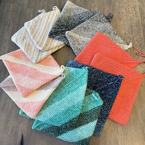 May include: A collection of nine crocheted dishcloths in various colors and patterns, including teal, pink, gray, and red. The dishcloths are made with a textured stitch and are perfect for cleaning and drying dishes.
