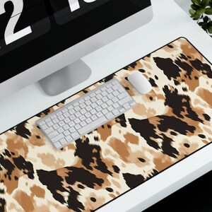 May include: A brown and black animal print desk mat with a white keyboard and a white mouse on top of it. The desk mat is on a white desk with a black computer monitor displaying the time 2:16 PM.