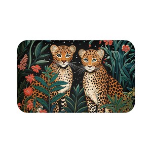 May include: A rectangular bath mat featuring two leopards with spotted fur, set against a backdrop of lush green foliage and vibrant orange flowers. The leopards have light blue eyes and are surrounded by a dark background with white speckles.