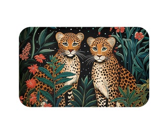 May include: A rectangular bath mat featuring two leopards with spotted fur, set against a backdrop of lush green foliage and vibrant orange flowers. The leopards have light blue eyes and are surrounded by a dark background with white speckles.