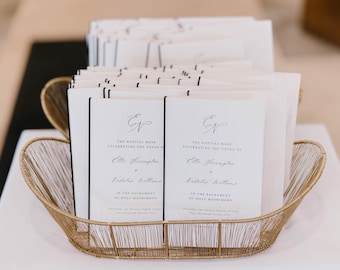 Peut inclure: Un panier doré en fil de fer contient des piles de programmes de cérémonie de mariage. Les programmes sont blancs avec du texte noir et une bordure noire. Le texte comprend les noms du couple et la date du mariage. Le panier repose sur une surface blanche.