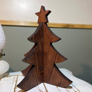 May include: A wooden Christmas tree decoration with a star on top. The tree is made of stained wood and has a rustic appearance. The tree is approximately 12 inches tall and is designed to stand on a flat surface.