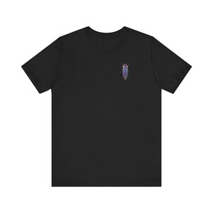 Puede incluir: Camiseta negra con un pequeño diseño de insecto colorido en el pecho. El insecto tiene un cuerpo largo y delgado con acentos morados, azules y verdes. La camiseta está hecha de un material suave y tiene mangas cortas.
