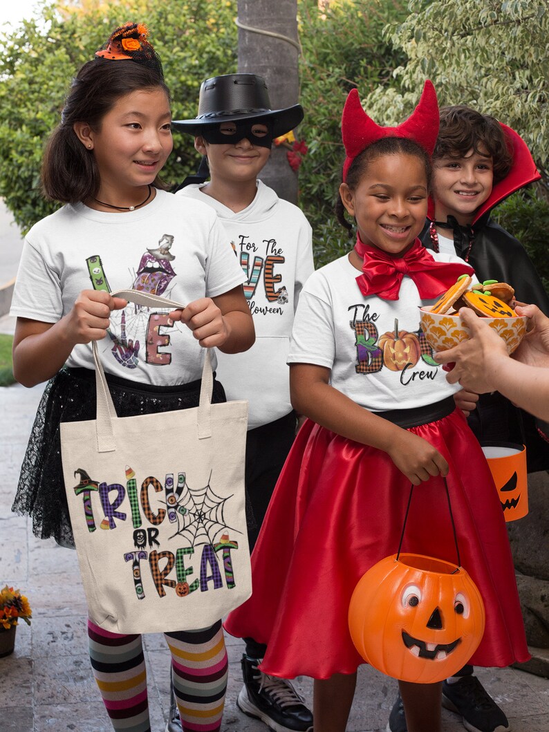 May include: Four children dressed in Halloween costumes, holding trick-or-treat bags and candy. The girl on the left is wearing a white shirt with the word "LOVE" in colorful letters, a witch hat, and a striped skirt. The boy in the middle is wearing a black cowboy hat, a black mask, and a white shirt with the words "For the LOVE Halloween". The girl on the right is wearing a red devil costume with horns and a red skirt. The boy on the far right is wearing a vampire costume with a black cape. The girl on the left is holding a white canvas tote bag with the words "Trick or Treat" in colorful letters.