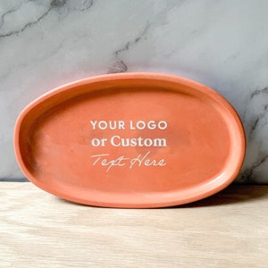May include: A light orange oval-shaped tray with a raised rim. The tray has white text that reads "YOUR LOGO or Custom Text Here".