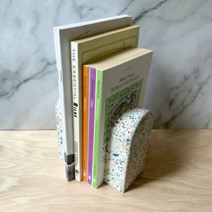 This arch bookend is perfect for adding style to any mantel, dresser, or desk or for using as book ends. The images show the white terrazzo style, which also comes in navy, hunter green, or beige. Each terrazzo piece is unique. Made of gypsum cement