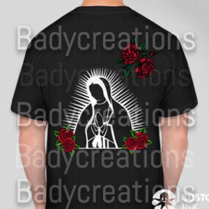 May include: Black t-shirt featuring a white graphic of the Virgin Mary with a halo and red roses. The design is centered on the back of the shirt. The text "Badycreations" is repeated vertically on the shirt.