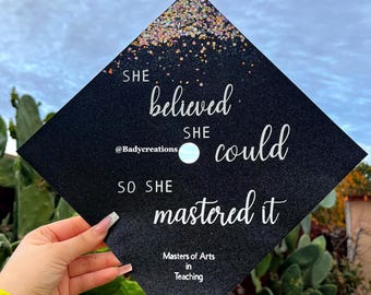 May include: Black graduation cap with silver glitter and the text "She believed she could so she mastered it" and "Masters of Arts in Teaching".