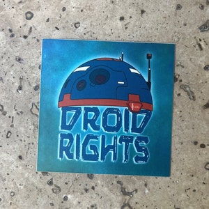 May include: A blue and red droid with the text "DROID RIGHTS" in a blue, distressed font on a teal background.