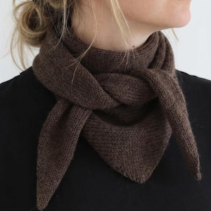 May include: A brown knitted scarf is wrapped around a person's neck. The scarf is a triangular shape with a twisted knot in the front. The scarf is made of a soft, textured material and is a solid brown color.