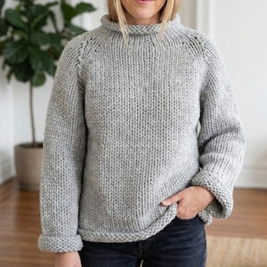K&ouml;nnte beinhalten: Ein hellgrauer, grob gestrickter Pullover mit hohem, geripptem Kragen und umgeschlagenen Manschetten. Der Pullover hat eine lockere Passform und ein schlichtes, klassisches Design. Die &Auml;rmel sind lang und der Saum ist gerade.