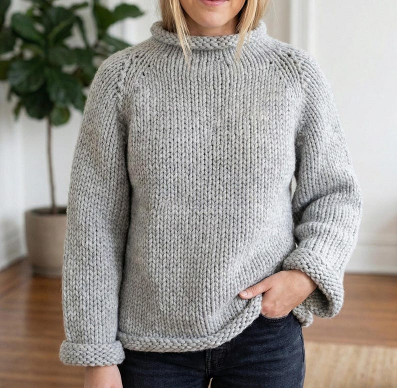 K&ouml;nnte beinhalten: Ein hellgrauer, grob gestrickter Pullover mit hohem, geripptem Kragen und umgeschlagenen Manschetten. Der Pullover hat eine lockere Passform und ein schlichtes, klassisches Design. Die &Auml;rmel sind lang und der Saum ist gerade.