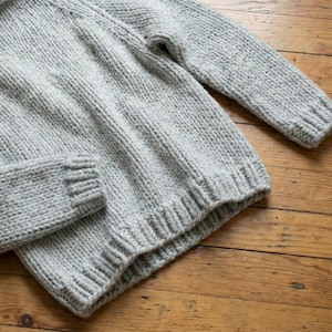 K&ouml;nnte beinhalten: Ein hellgrauer Strickpullover mit gerippten B&uuml;ndchen und Saum. Der Pullover hat lange &Auml;rmel und einen Rundhalsausschnitt. Der Strickstoff hat ein strukturiertes Aussehen. Der Pullover ist aus einem weichen, warmen Material gefertigt.