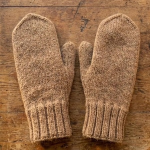 May include: A pair of knitted mittens in a warm, earthy brown hue. The mittens have a ribbed cuff and a classic mitten shape, perfect for keeping hands warm. The textured knit adds a cozy, handmade feel.