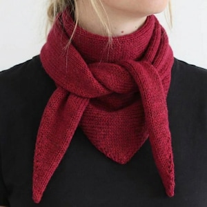 Pode incluir: Cachecol de malha bordô amarrado na frente, drapeado ao redor do pescoço. O cachecol tem formato triangular na parte inferior e é feito de um fio macio e texturizado. O cachecol é usado sobre uma camisa preta.