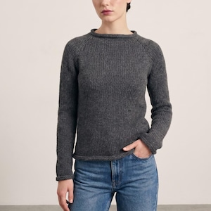 May include: A charcoal grey long-sleeve jumper featuring a ribbed knit texture, a round neckline, and raglan sleeves. The jumper is paired with blue denim jeans, which have a classic five-pocket design and a standard button and zip closure.