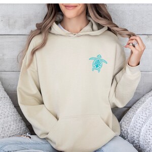 May include: A light beige hoodie with a blue and white patterned sea turtle design on the front.