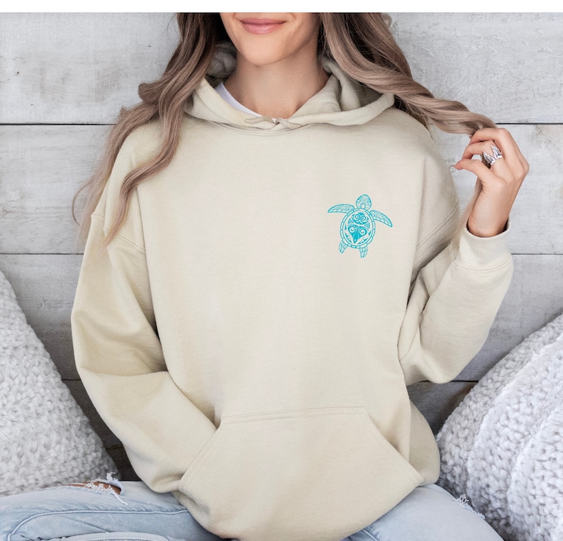 May include: A light beige hoodie with a blue and white patterned sea turtle design on the front.