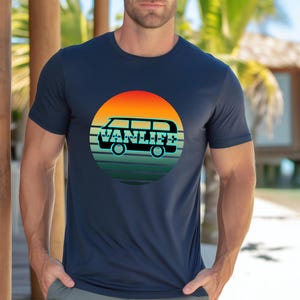 Peut inclure: T-shirt bleu marine avec un motif circulaire repr&eacute;sentant un van et le texte "VANLIFE". Le motif pr&eacute;sente un coucher de soleil avec des teintes orange, jaune et verte. Le t-shirt est de style col rond.